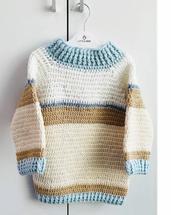 A cozy handmade crochet sweater for kids, crafted from soft breathable cotton yarn. Perfect for mild winters and everyday wear. Keep your little one warm and stylish with this handmade crochet kids sweater, thoughtfully crafted using soft, breathable cotton yarn. Designed for comfort and durability, this pullover features a classic striped pattern in neutral tones, making it suitable for both boys and girls. The sweater is lightweight yet warm, ideal for mild winter weather, air-conditioned environments, or evening outings. Ribbed cuffs, neckline, and hem provide a snug fit while allowing easy movement for active kids. Each piece is carefully handmade, ensuring quality craftsmanship and a unique finish. A perfect choice for daily wear, gifting, or special occasions.